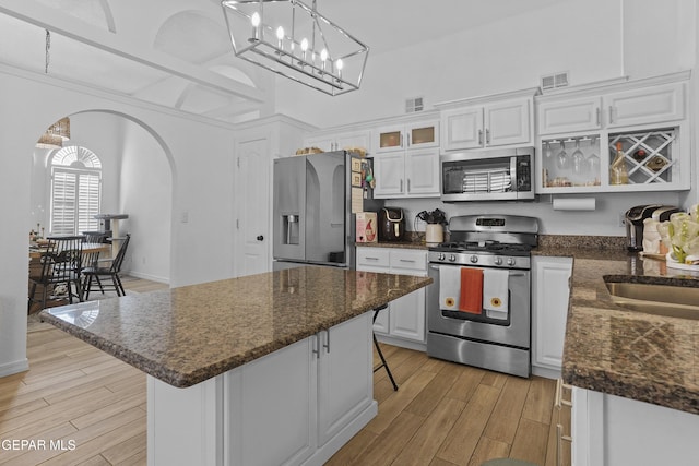 11973 Regal Banner Ln, El Paso, TX 79936 - kitchen featuring stainless steel appliances, arched walkways, white cabinetry, light wood-style flooring, and a kitchen bar