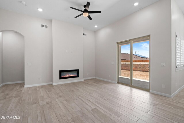 13351 Jeff Winton Dr, El Paso, TX 79928 - unfurnished living room featuring light wood-style floors, a ceiling fan, a glass covered fireplace, arched walkways, and recessed lighting
