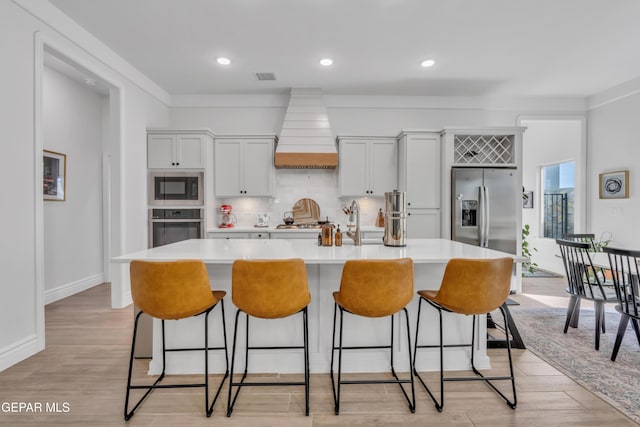 13107 Kington Ave, El Paso, TX 79928 - kitchen with stainless steel appliances, custom range hood, a center island with sink, light countertops, and light wood-style flooring