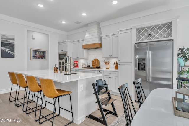 13107 Kington Ave, El Paso, TX 79928 - kitchen featuring premium range hood, appliances with stainless steel finishes, light wood-style flooring, a breakfast bar, and an island with sink