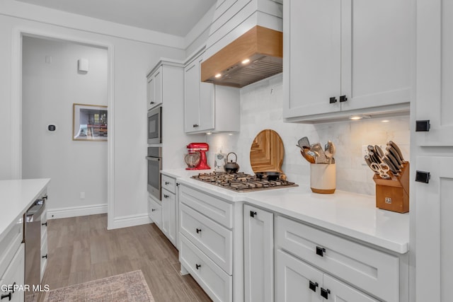 13107 Kington Ave, El Paso, TX 79928 - kitchen featuring appliances with stainless steel finishes, custom range hood, decorative backsplash, light countertops, and light wood-type flooring
