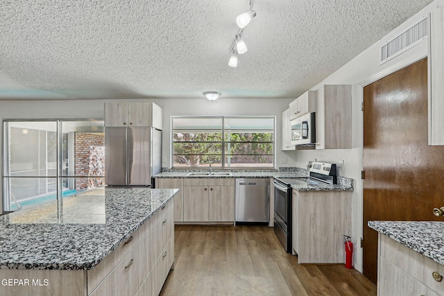 9204 Rex Ct, El Paso, TX 79925 - kitchen featuring appliances with stainless steel finishes, a textured ceiling, a sink, wood finished floors, and light stone counters