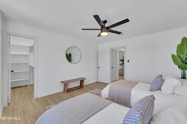 11316 Menlo Ave, El Paso, TX 79936 - bedroom featuring a walk in closet, light wood-style floors, baseboards, a ceiling fan, and a textured ceiling