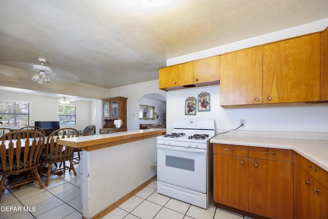 113 N Moon Rd, Socorro, TX 79927 - kitchen with white range with gas stovetop, arched walkways, light countertops, light tile patterned floors, and a textured ceiling