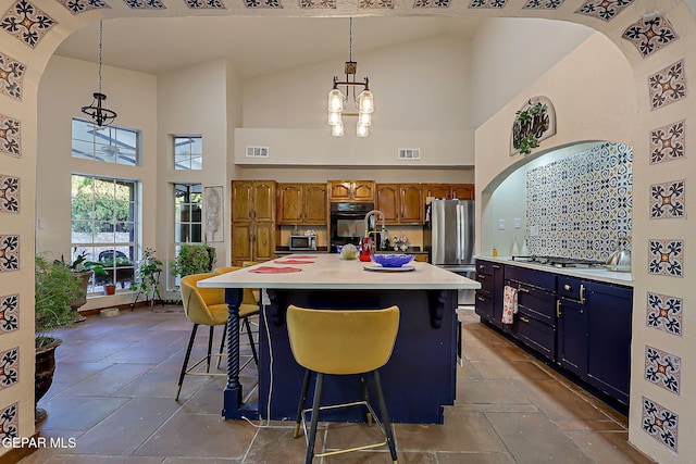 6112 Strahan Rd, El Paso, TX 79932 - kitchen with high vaulted ceiling, stainless steel appliances, brown cabinetry, a chandelier, and light countertops