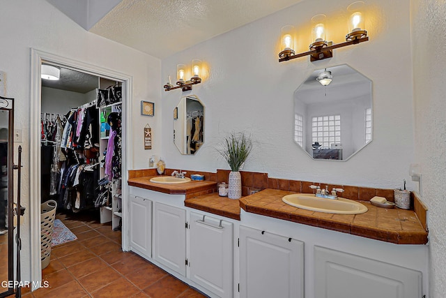 6112 Strahan Rd, El Paso, TX 79932 - bathroom featuring double vanity, tile patterned flooring, a spacious closet, and a textured ceiling
