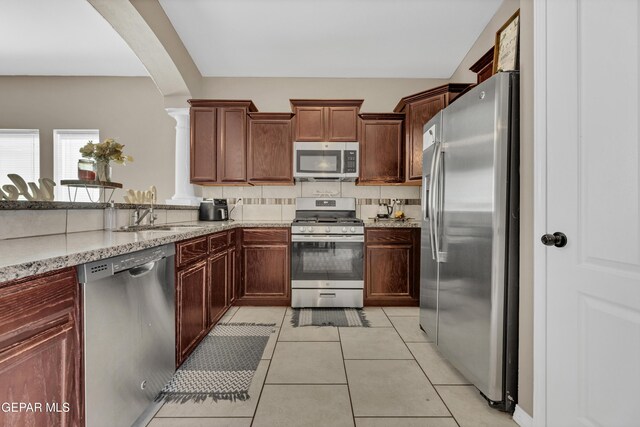 14250 Charles Pollock Ave, El Paso, TX 79938 - kitchen featuring stainless steel appliances, a sink, arched walkways, light stone counters, and light tile patterned floors