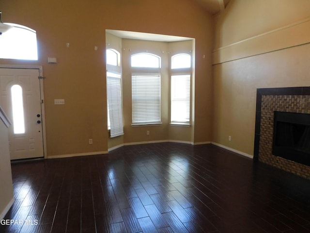 11233 Red Barrel Pl, El Paso, TX 79934 - unfurnished living room featuring wood finished floors, a tiled fireplace, a high ceiling, and baseboards