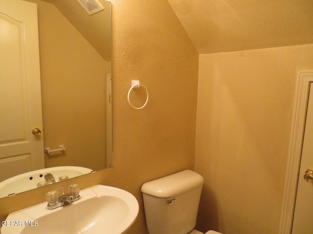 1679 Roger Bombach Dr, El Paso, TX 79936 - half bathroom featuring a sink, toilet, and vaulted ceiling