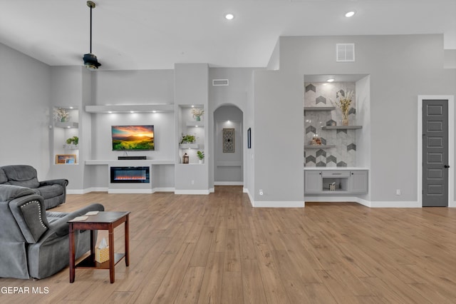 14405 Tierra Campeon, El Paso, TX 79938 - living room featuring arched walkways, built in features, light wood-style flooring, a glass covered fireplace, and baseboards