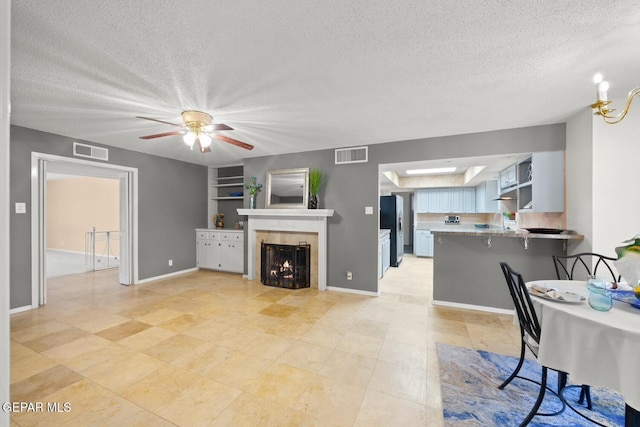 8820 Dirk Ct, El Paso, TX 79925 - living room featuring a textured ceiling, a tile fireplace, ceiling fan, built in shelves, and light tile patterned floors