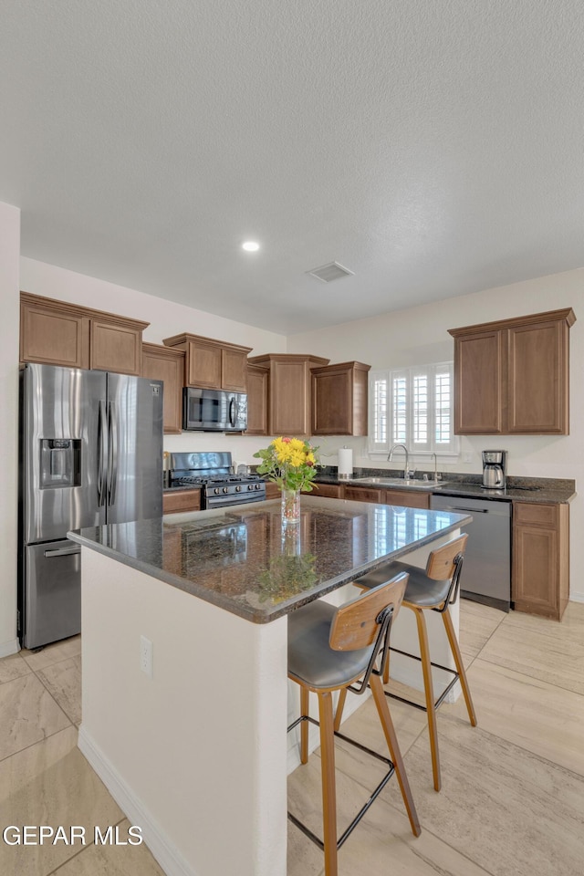 2201 Morning Mist Pl, El Paso, TX 79938 - kitchen featuring appliances with stainless steel finishes, a kitchen island, dark stone countertops, brown cabinetry, and a kitchen breakfast bar