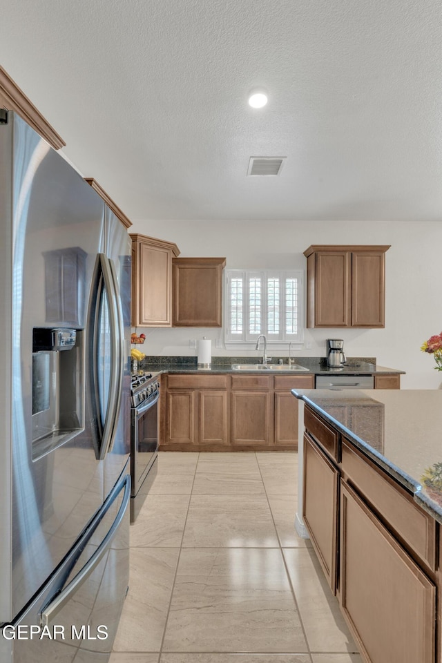 2201 Morning Mist Pl, El Paso, TX 79938 - kitchen with appliances with stainless steel finishes, a sink, a textured ceiling, dark stone counters, and brown cabinets
