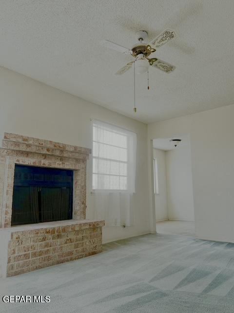 2520 San Jose Ave Unit 2D, El Paso, TX 79930 - unfurnished living room with carpet floors, a textured ceiling, a brick fireplace, and a ceiling fan