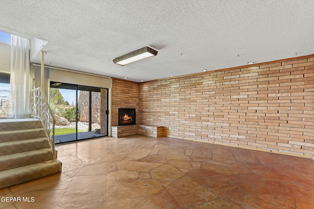 3134 Mesa Verde Ln, El Paso, TX 79904 - unfurnished living room featuring brick wall, stone flooring, stairway, a fireplace, and a textured ceiling