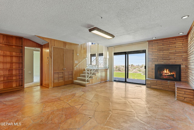 3134 Mesa Verde Ln, El Paso, TX 79904 - unfurnished living room featuring stone flooring, built in features, stairway, wooden walls, and a brick fireplace