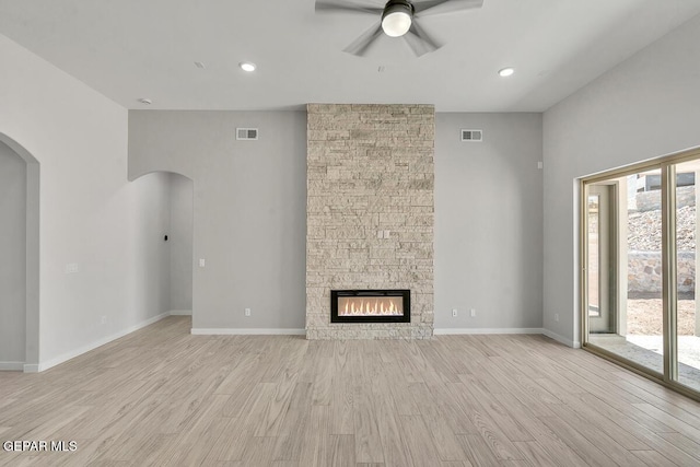 248 Emerald Storm Pl, El Paso, TX 79928 - unfurnished living room with a ceiling fan, arched walkways, light wood-style flooring, a stone fireplace, and baseboards