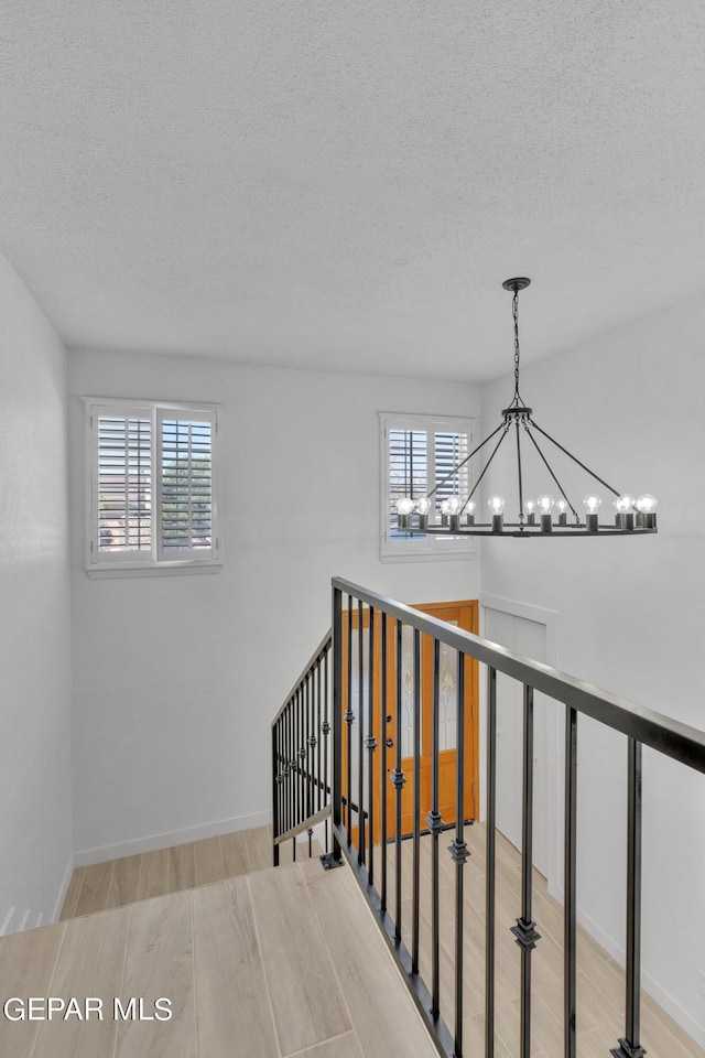 1460 Backus St, El Paso, TX 79925 - staircase featuring a chandelier, a textured ceiling, wood finished floors, plenty of natural light, and baseboards