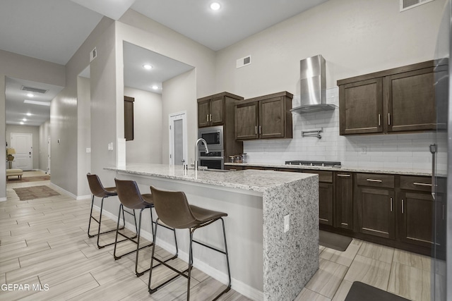 2305 Enchanted Quail, El Paso, TX 79911 - kitchen with wall chimney range hood, appliances with stainless steel finishes, a breakfast bar area, dark brown cabinets, and recessed lighting