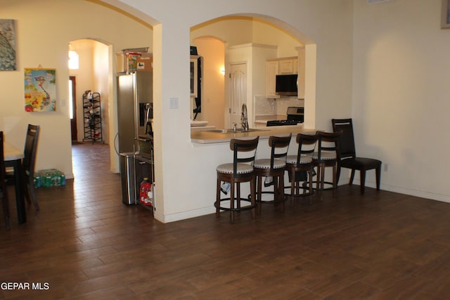 1429 Jettie Ray Way, El Paso, TX 79936 - kitchen with stainless steel appliances, a breakfast bar, dark wood finished floors, arched walkways, and tasteful backsplash