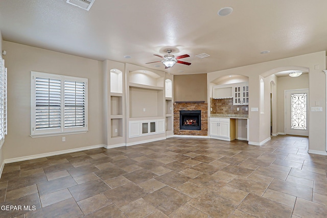 3841 Tierra Campa Dr, El Paso, TX 79938 - unfurnished living room featuring a ceiling fan, built in shelves, a fireplace, arched walkways, and stone finish floors