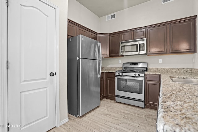14391 Loma Esmeralda, El Paso, TX 79938 - kitchen with appliances with stainless steel finishes, light wood finished floors, dark brown cabinetry, and light stone counters