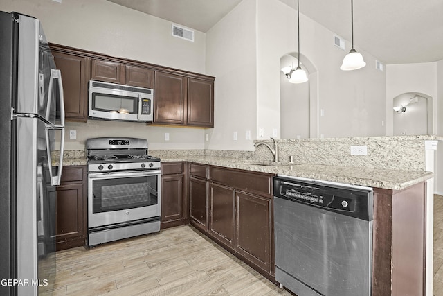 14391 Loma Esmeralda, El Paso, TX 79938 - kitchen with appliances with stainless steel finishes, light wood-style floors, a peninsula, dark brown cabinets, and light stone counters