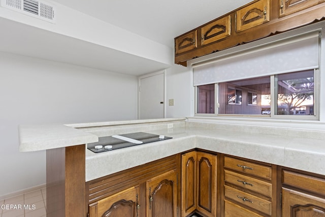 408 Spring Hill Cir, El Paso, TX 79912 - kitchen with black electric cooktop, light countertops, a peninsula, brown cabinetry, and light tile patterned flooring