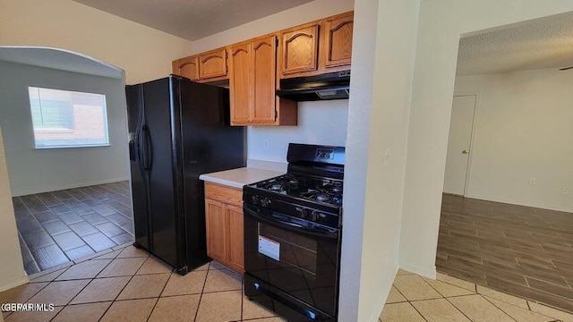 3541 Al Roberts Dr, El Paso, TX 79936 - kitchen with black appliances, under cabinet range hood, light tile patterned floors, light countertops, and brown cabinetry