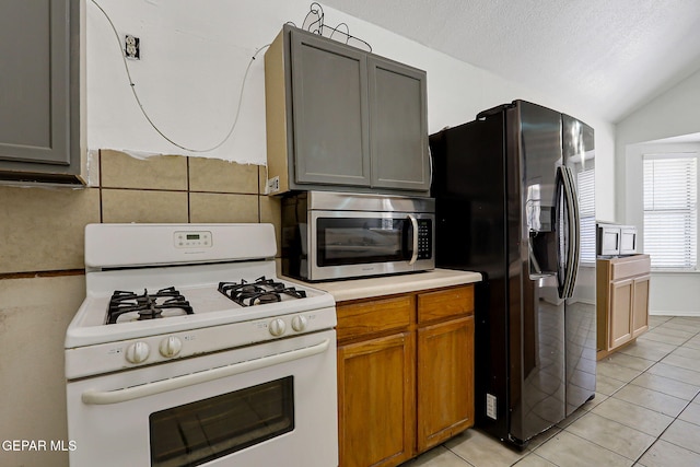 11364 Crater Lake Ave, El Paso, TX 79936 - kitchen with white gas stove, stainless steel microwave, black refrigerator with ice dispenser, light tile patterned floors, and light countertops