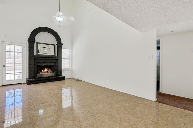 11364 Crater Lake Ave, El Paso, TX 79936 - unfurnished living room with a large fireplace, a textured ceiling, tile patterned flooring, a high ceiling, and baseboards