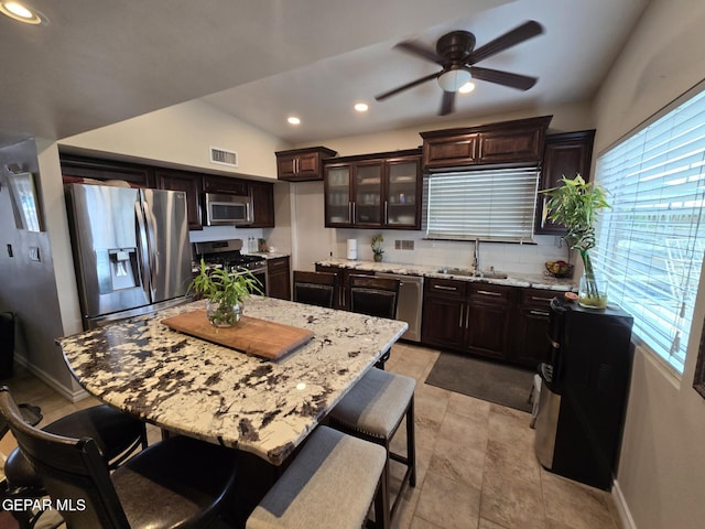 7000 Armistad Ave, El Paso, TX 79912 - kitchen featuring appliances with stainless steel finishes, ceiling fan, dark brown cabinets, a kitchen breakfast bar, and light stone countertops
