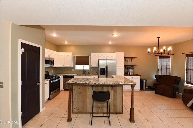 12712 Tierra Aurora Dr, El Paso, TX 79938 - kitchen with appliances with stainless steel finishes, white cabinets, a kitchen bar, a chandelier, and light tile patterned floors