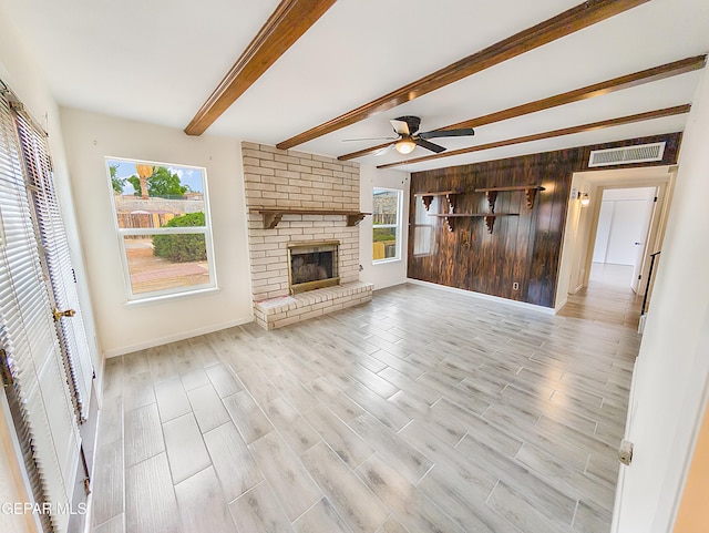 3425 Dialrock Ln, El Paso, TX 79935 - unfurnished living room with healthy amount of natural light, a ceiling fan, beam ceiling, a fireplace, and light wood-style flooring