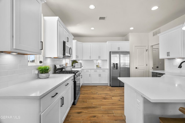 905 Bilton Pl, El Paso, TX 79928 - kitchen featuring appliances with stainless steel finishes, wood finished floors, tasteful backsplash, white cabinets, and recessed lighting