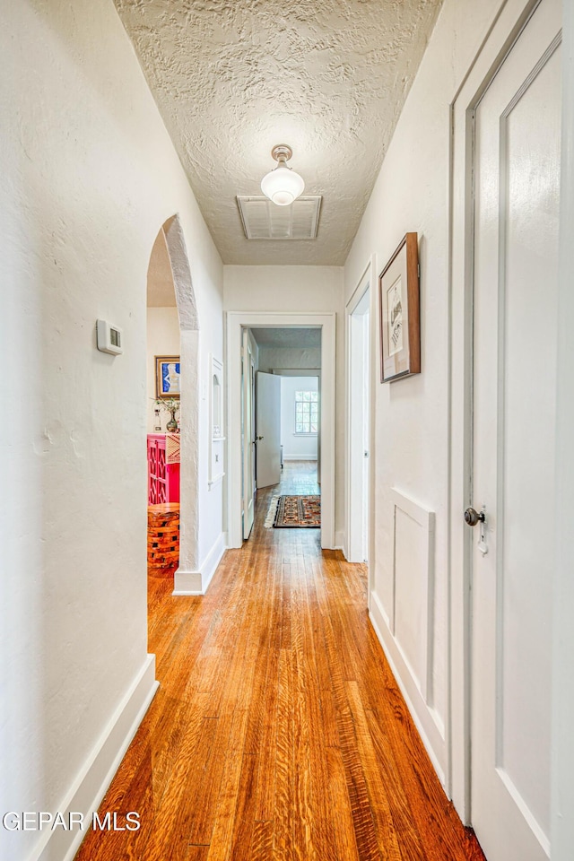 4021 Hastings Dr, El Paso, TX 79903 - hallway with arched walkways, light wood finished floors, and a textured ceiling