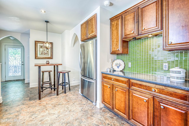 4021 Hastings Dr, El Paso, TX 79903 - kitchen featuring freestanding refrigerator, arched walkways, brown cabinets, dark countertops, and decorative backsplash