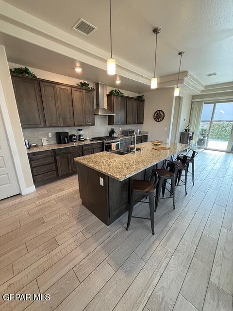 2313 Dancing Piper Way, El Paso, TX 79911 - kitchen featuring wall chimney range hood, light wood-type flooring, a breakfast bar, and dark brown cabinetry