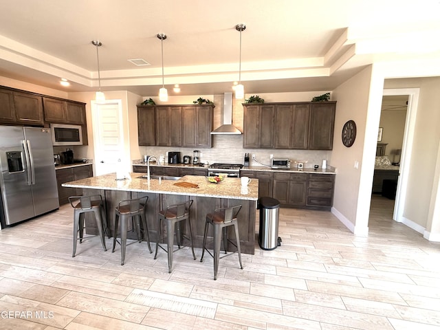 2313 Dancing Piper Way, El Paso, TX 79911 - kitchen with appliances with stainless steel finishes, wall chimney range hood, a tray ceiling, and a breakfast bar