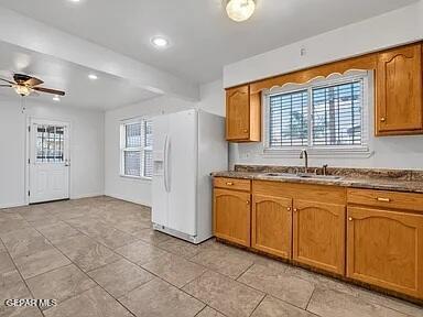 3305 Killarney St, El Paso, TX 79925 - kitchen featuring white fridge with ice dispenser, brown cabinetry, a ceiling fan, light tile patterned floors, and dark countertops