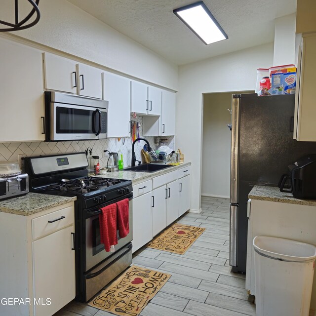 5028 Sagittarius Ave, El Paso, TX 79924 - kitchen with appliances with stainless steel finishes, backsplash, light countertops, white cabinetry, and wood tiled floors