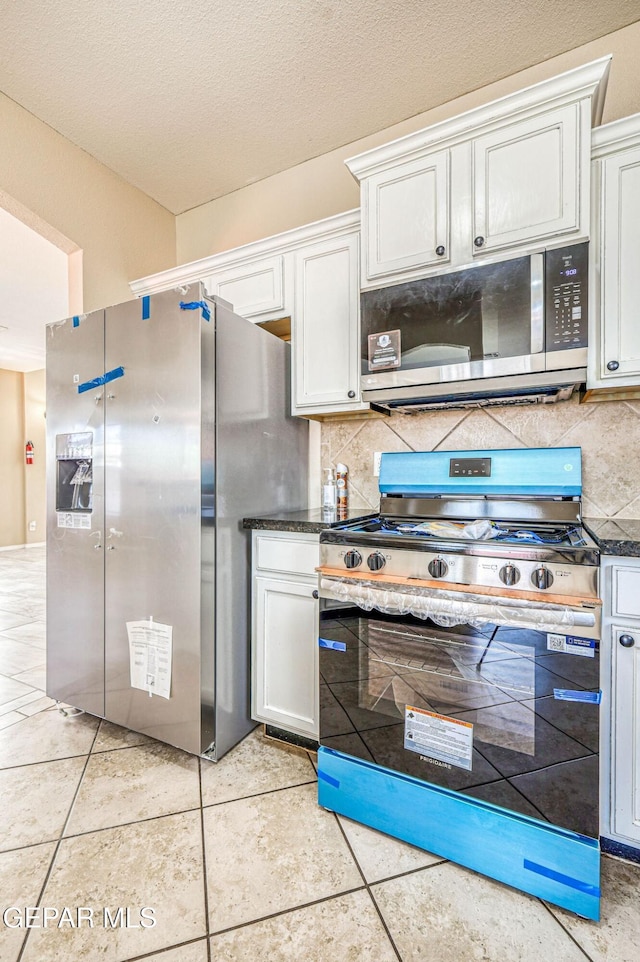 14376 N Cave Dr, El Paso, TX 79938 - kitchen with stainless steel appliances, tasteful backsplash, dark countertops, light tile patterned flooring, and white cabinets