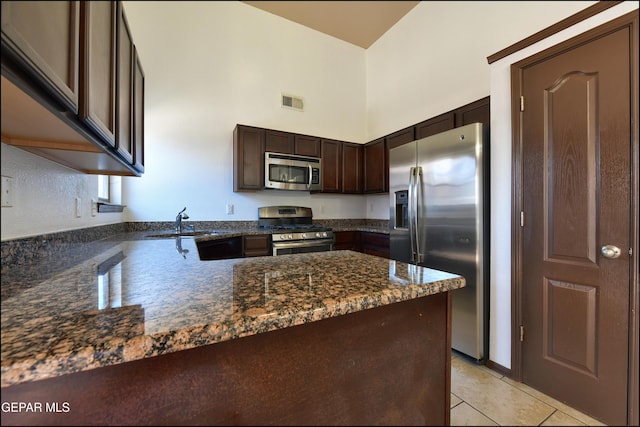 4908 Gold Ranch Ave, El Paso, TX 79934 - kitchen featuring appliances with stainless steel finishes, dark brown cabinetry, dark stone counters, a peninsula, and a towering ceiling