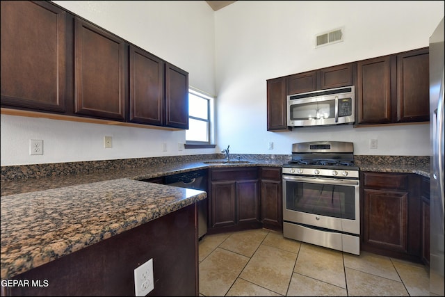 4908 Gold Ranch Ave, El Paso, TX 79934 - kitchen featuring stainless steel appliances, light tile patterned floors, dark brown cabinetry, dark stone counters, and a towering ceiling