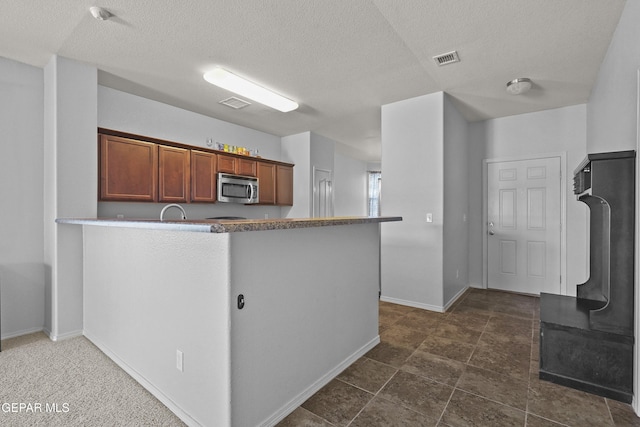 14477 Jacinto Ramos Ave, El Paso, TX 79938 - kitchen with stainless steel microwave, a textured ceiling, a peninsula, and brown cabinets