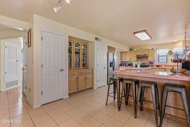 9769 Galilee Dr, El Paso, TX 79927 - kitchen featuring stainless steel appliances, a peninsula, a kitchen bar, light tile patterned floors, and under cabinet range hood
