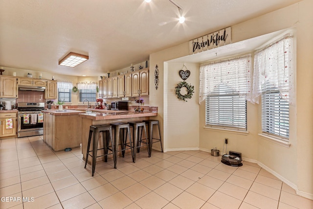 9769 Galilee Dr, El Paso, TX 79927 - kitchen featuring stainless steel gas range, a peninsula, light tile patterned floors, a kitchen bar, and light brown cabinets