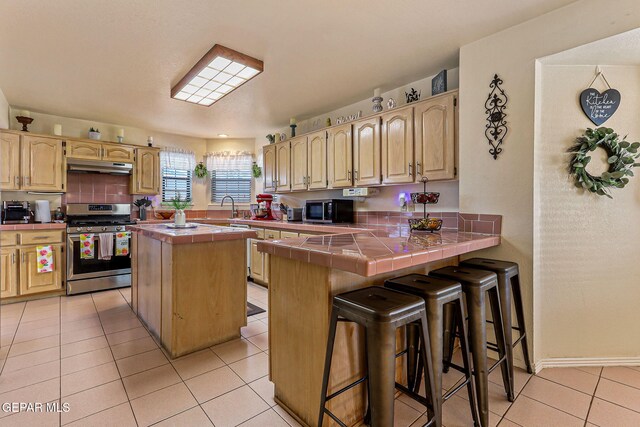 9769 Galilee Dr, El Paso, TX 79927 - kitchen featuring stainless steel gas stove, tile countertops, black microwave, under cabinet range hood, and a peninsula