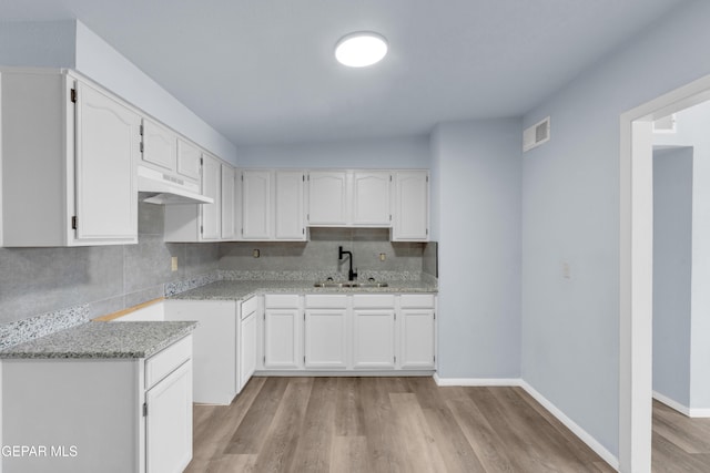 231 Romeria Dr, El Paso, TX 79907 - kitchen with under cabinet range hood, tasteful backsplash, white cabinetry, and light wood-type flooring