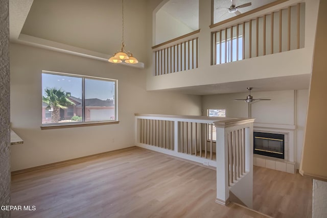 3148 Tierra Encino Dr, El Paso, TX 79938 - empty room with ceiling fan, wood finished floors, a high ceiling, a tiled fireplace, and a chandelier